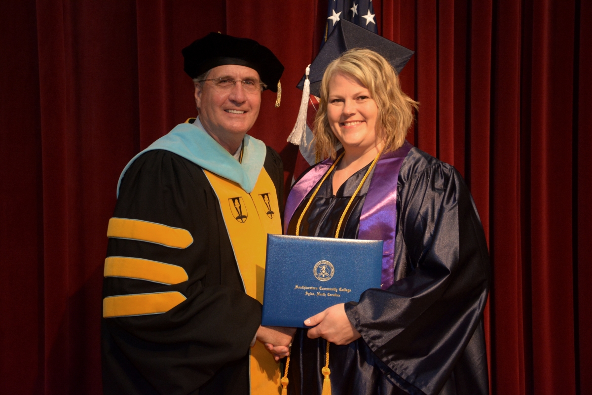 Woman wearing graduation cap & gown receives credential from man.