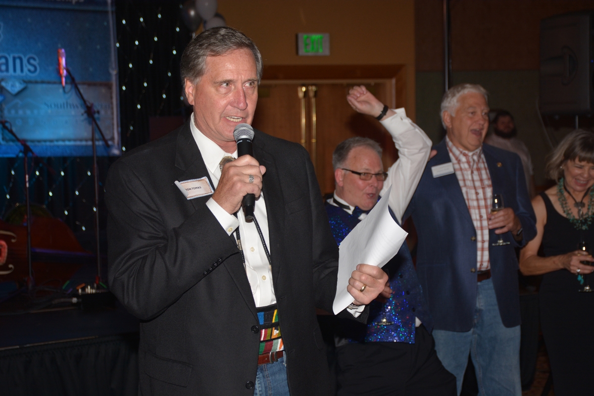 Man speaks into a microphone as others celebrate behind him