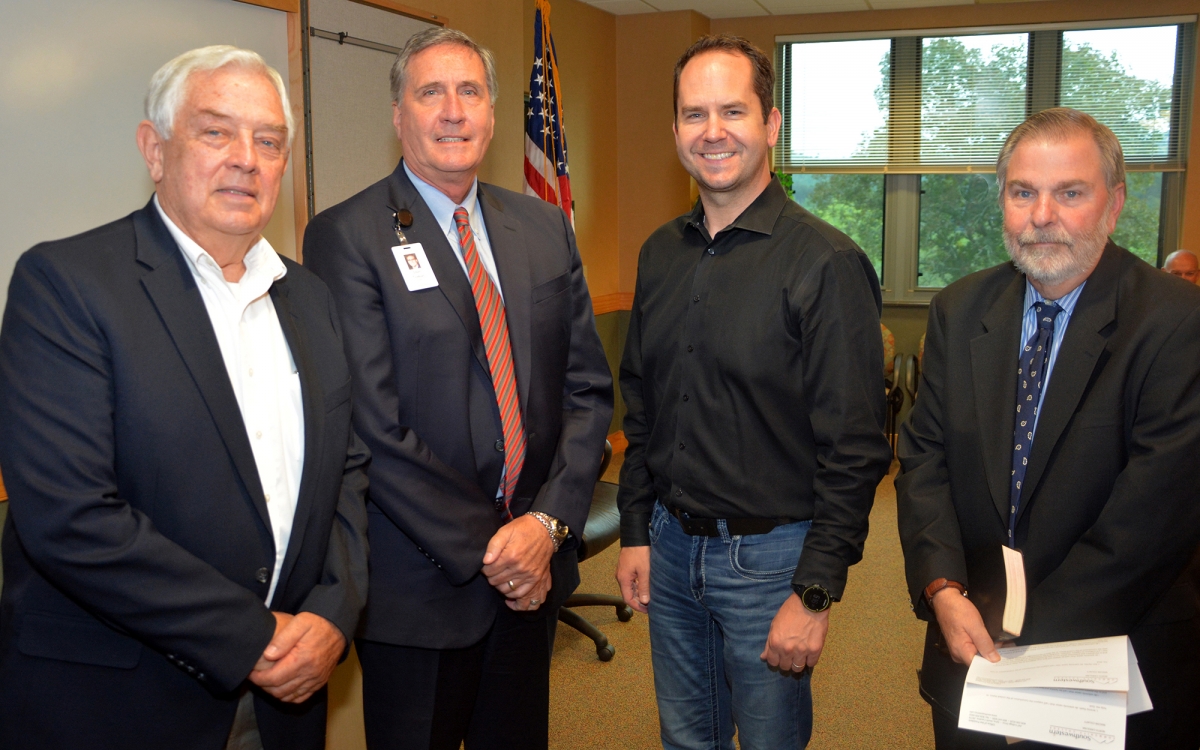 Four men pose inside a board room