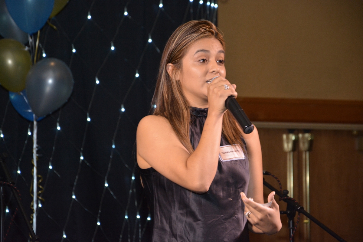 Woman speaks into a microphone on stage at gala.