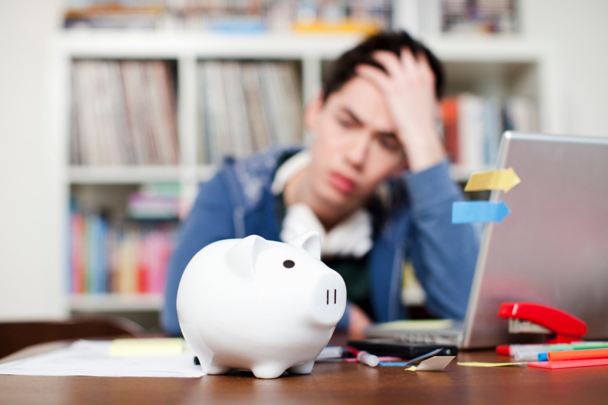 Student holds his hand to his head and looks depressed as he stares at a piggy bank