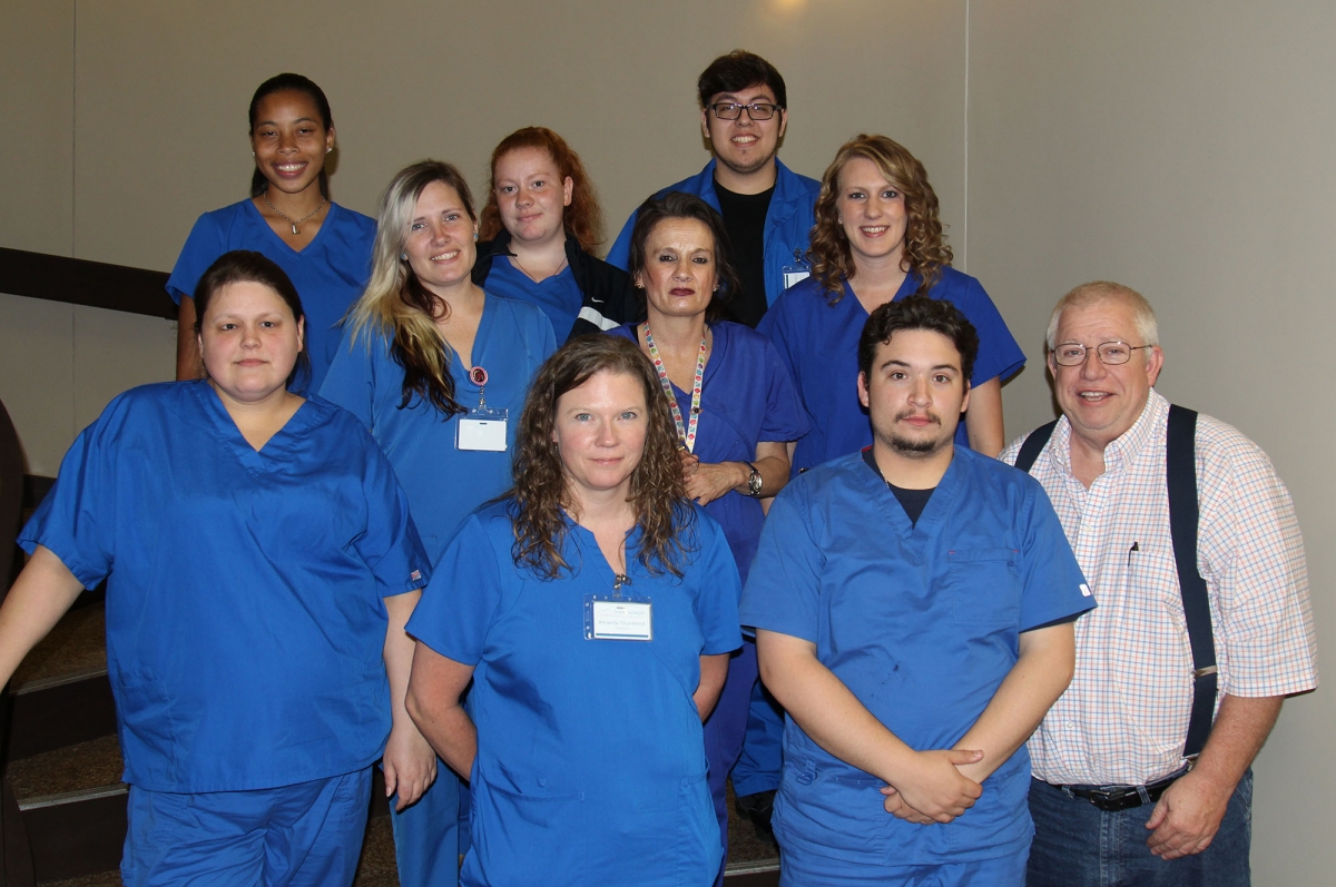 Ten students wearing blue scrubs stand with their professor on a stairway inside a building on SCC's Jackson Campus.