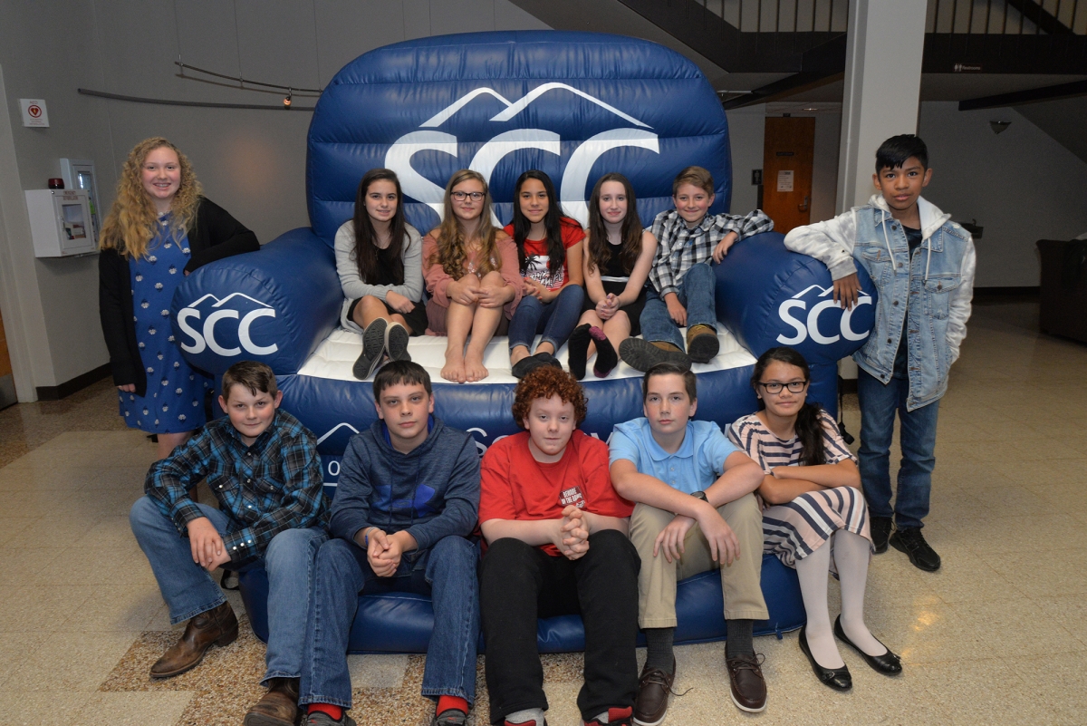 More than a dozen students pose on a blue inflatable chair with SCC logos.
