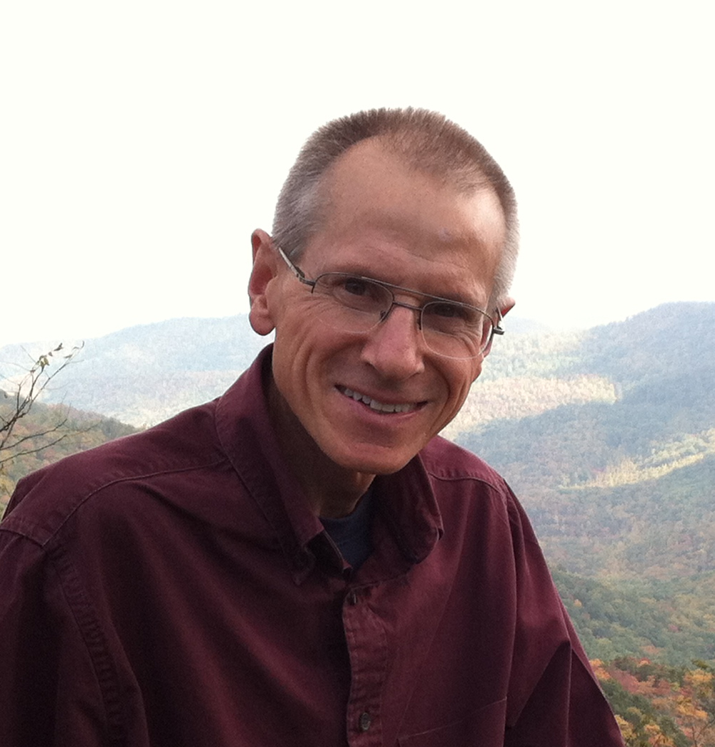 Man stands in foreground; behind him is mountain scenery