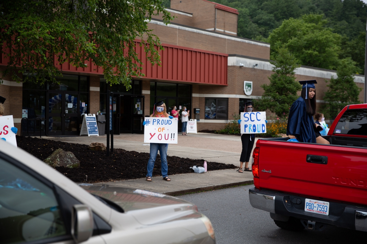 Cars carry graduates past cheering faculty holding up signs