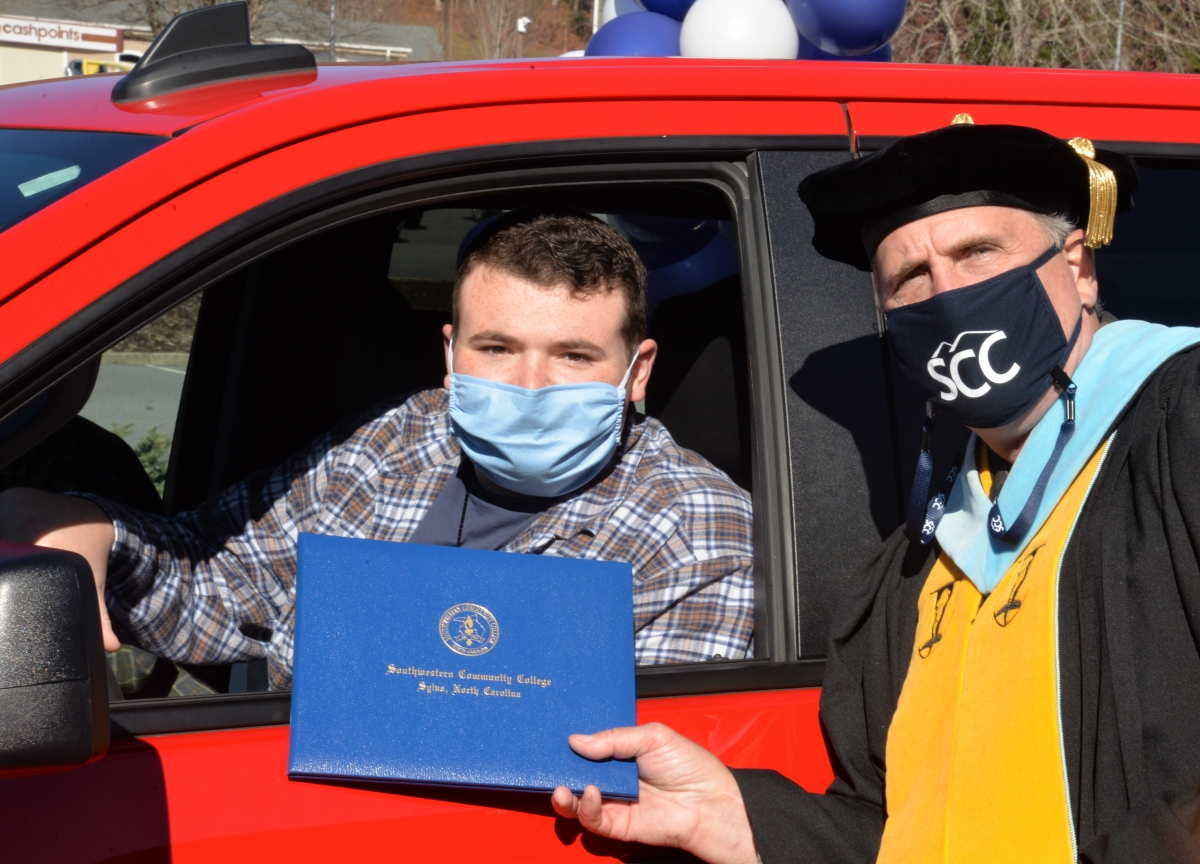 Cars carry graduates past cheering faculty holding up signs