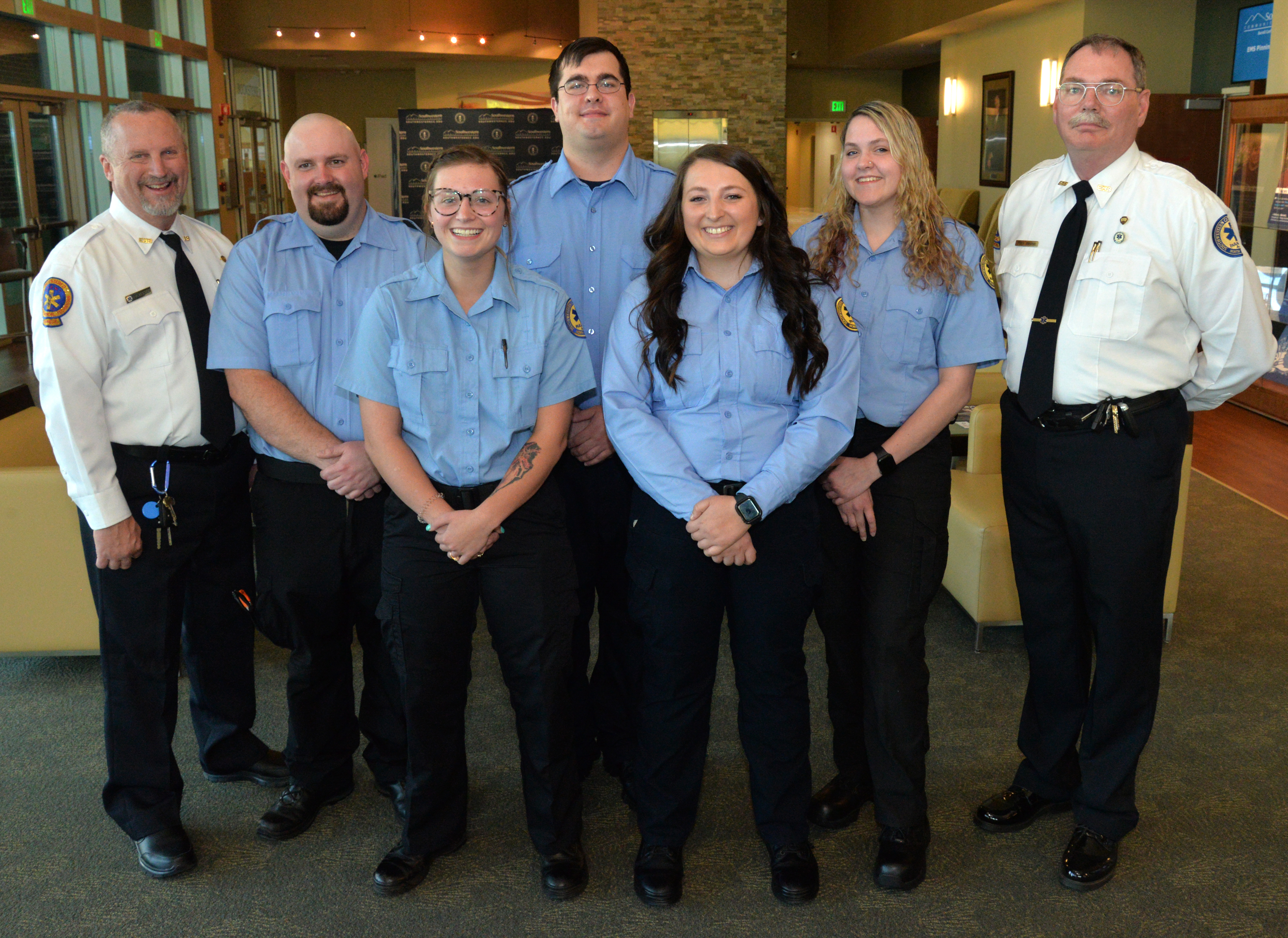 Five graduates stand beside their instructors