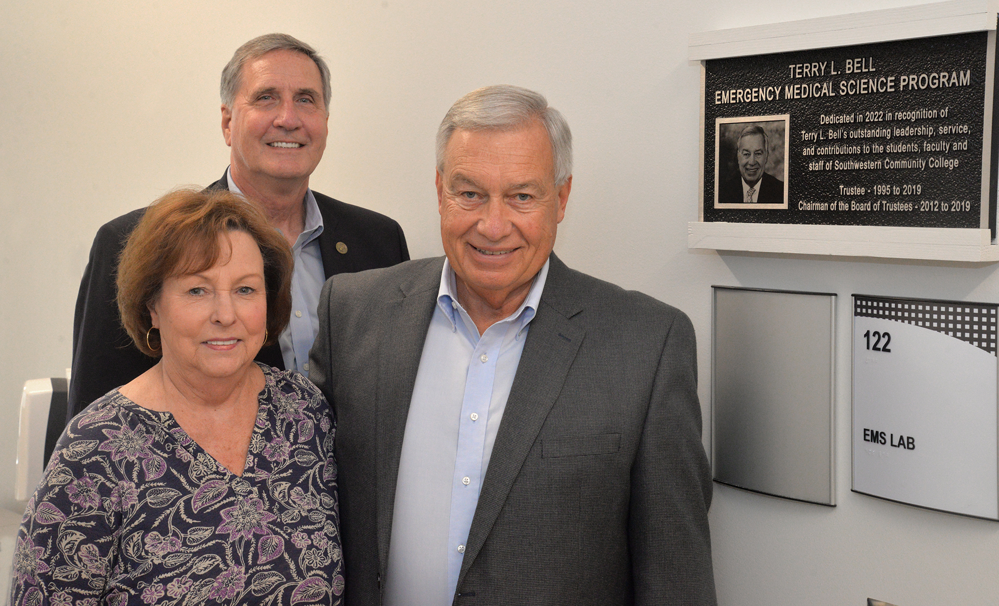 Three people stand beside a plaque