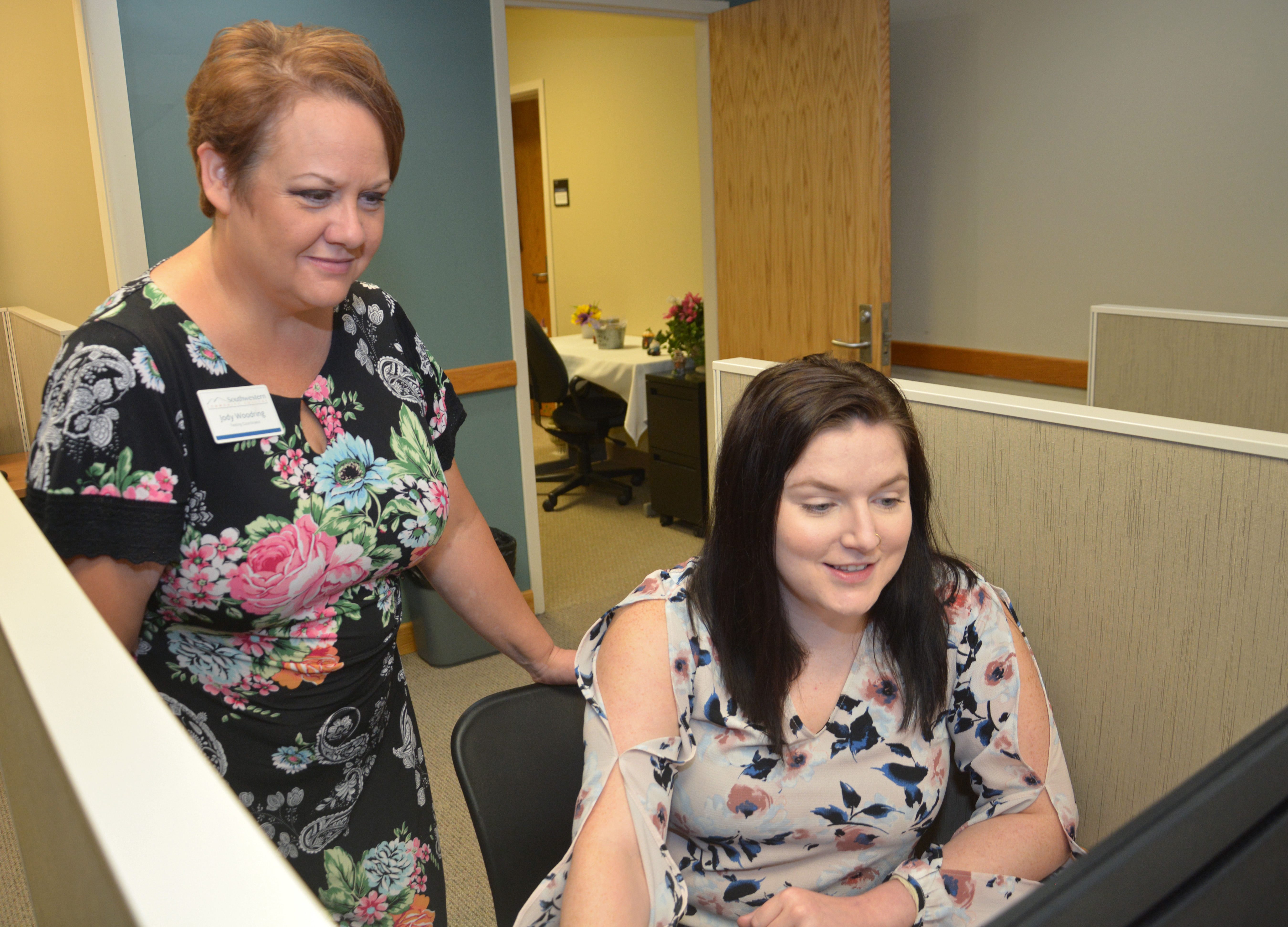 Standing woman guides seated woman through setting up a test on a computer at SCC