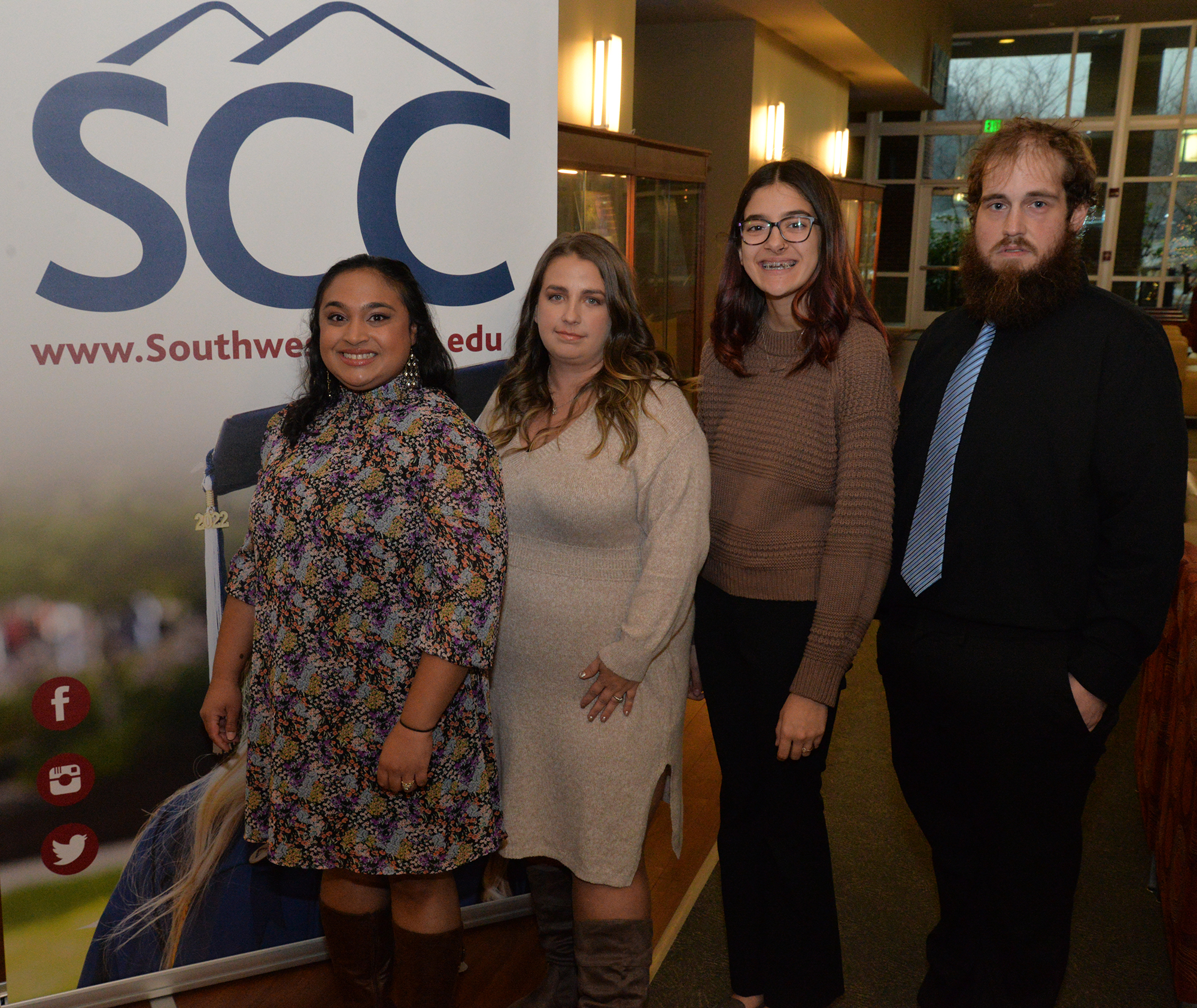 Four graduates stand beside SCC banner