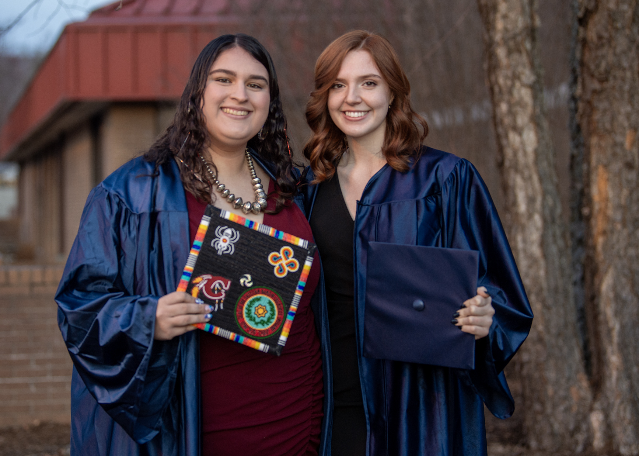 Two graduates smiling in front of the Balsam Center