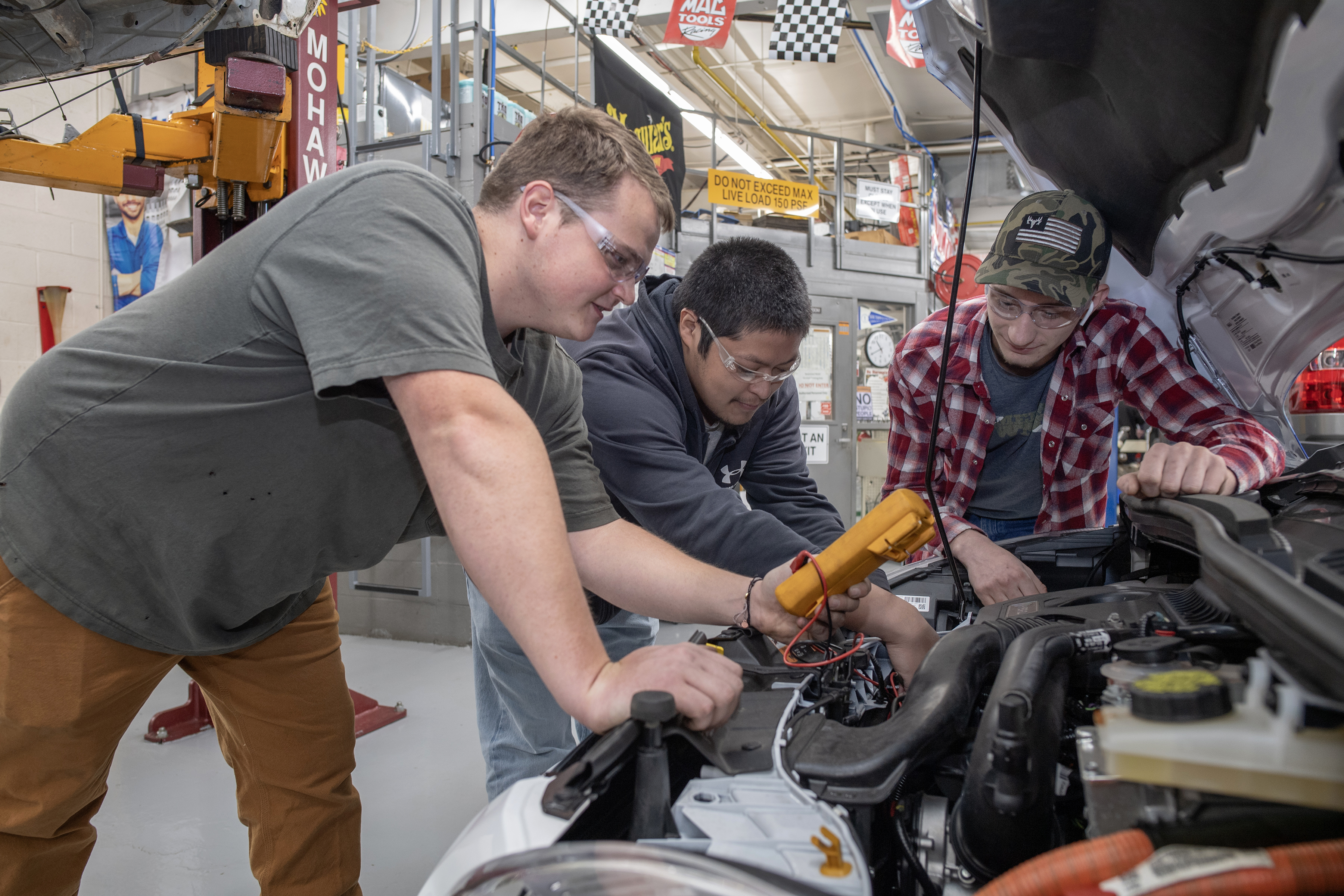 Three students look under the hood of a vehicle
