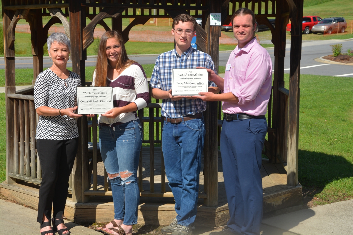 Two young students are holding scholarship certificates in front of gazebo.