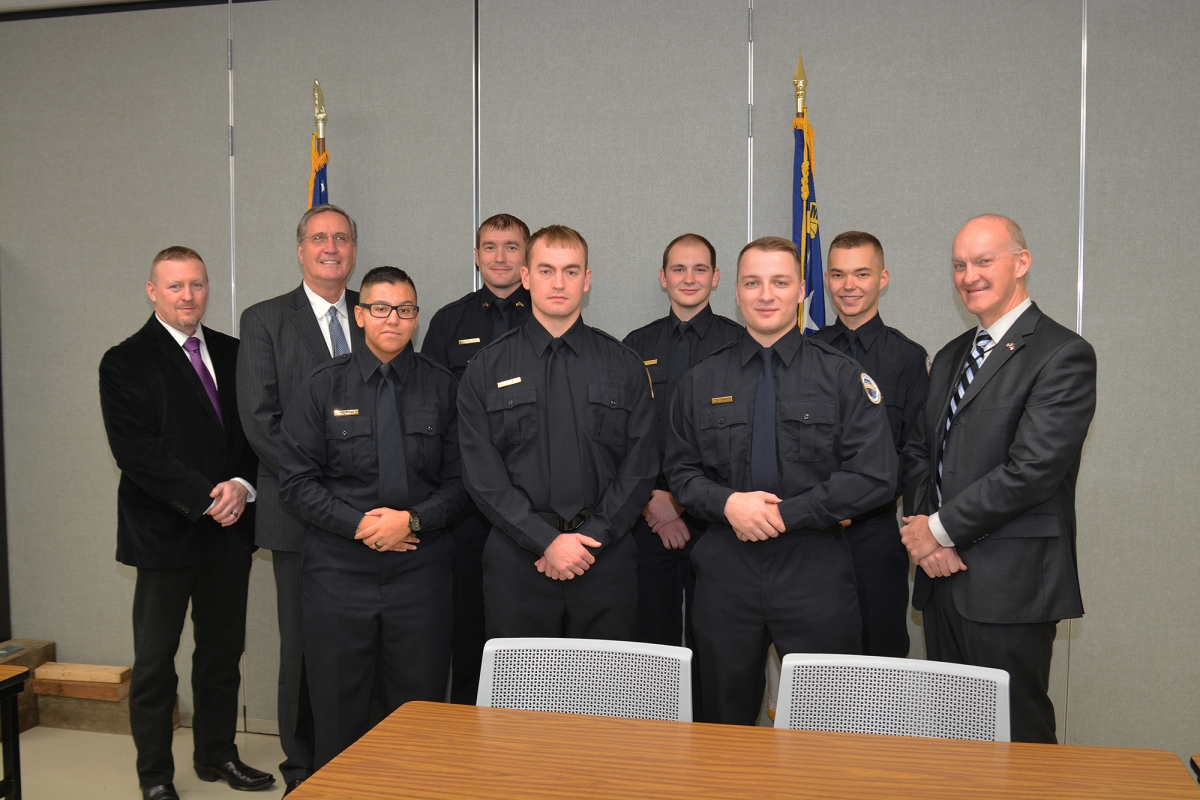 A group of law enforcement graduates huddle close in their uniforms beside administration members.