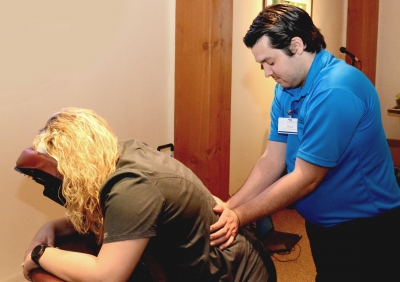 Young man from the Therapeutic Massage program provides a massage to a health fair attendee.