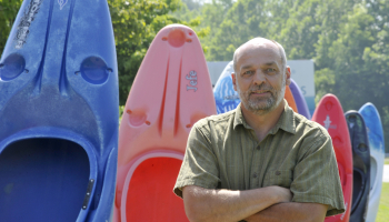 Man stands beside a row of kayaks outdoors