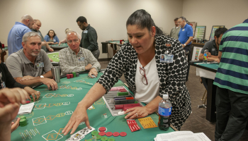 Woman deals a hand of blackjack to several classmates inside a casino training room.