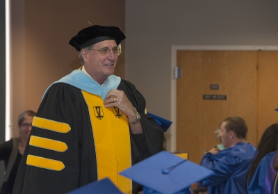 College president, wearing academic regalia, addresses graduates inside Balsam Center