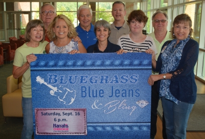 Group of people hold up sign that reads "Bluegrass, Blue Jeans & Bling" with the date "Sept. 16"
