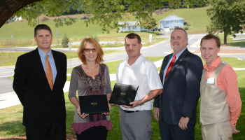 Students stand with SCC and SECU officials under a tree.