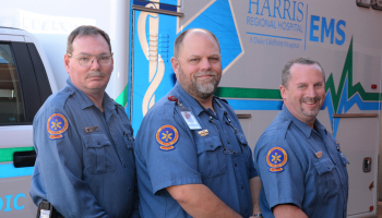 Three paramedics pose in front of a Harris Regional ambulance