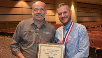 Student holding framed certificate poses with his instructor
