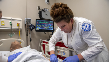 Female student inserts an IV into arm of a simulation mannequin