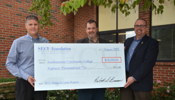 Three men hold up an oversized check