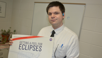 Man holds up a book cover entitled "Getting A Feel For Eclipses"