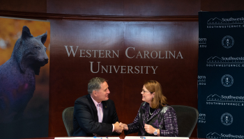 Dr. Brown &amp; Dr. Tomas shake hands at a board room table..