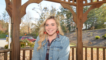 Young woman smiles underneath a gazebo on a sunny fall day.