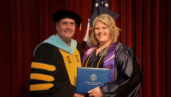Woman wearing cap and gown receives diploma from man.