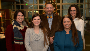 Five students pose in front of a Christmas tree.