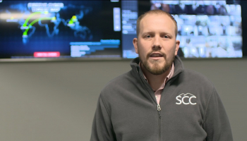 Man stands in front of flat screen displaying world map