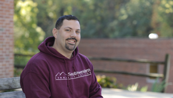 Man sits with SCC fall foliage in the background