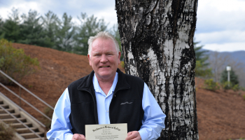 man poses outdoors with diploma