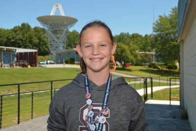 Female student poses in front of a radio telescope.