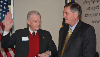 One man holds a Bible as the other places his left hand on the Bible and his right hand in the air to take an oath.
