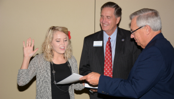 woman holds hand up and reads paper for two men