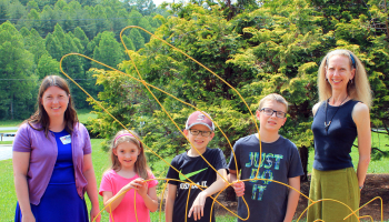 4-H students and Swain Center staff stand with bee sculpture in 4-H learning garden at SCC Swain Center.