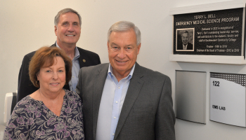 Three people stand beside a plaque