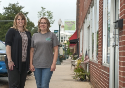Two women stand outdoors in downtown Sylva with the Jackson County courthouse in the distance behind them.