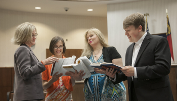 Female attorney stands with her students in a local court room reading legal books.