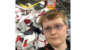 Man stands in front of robot; banner with text in Japanese language is in background