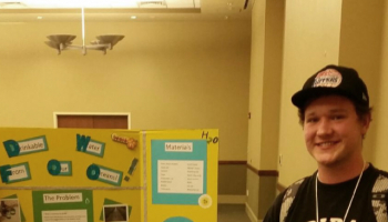 Jonah Caplinger holding first prize certificates standing next to his science project.