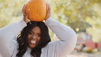 Student in gray sweatshirt holding pumpkin on top of her head.