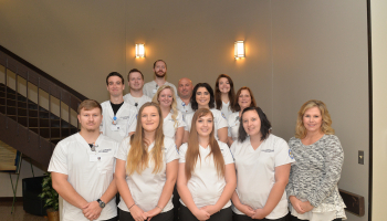 A group of first-year radiography students stand on a staircase in their uniforms alongside female instructor.