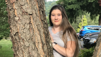 Young woman stands outside against a tree.