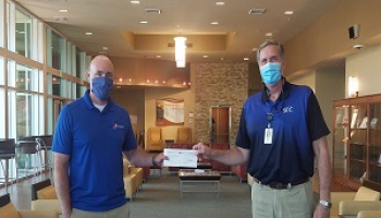 Two gentlemen shake hands while wearing masks and standing apart