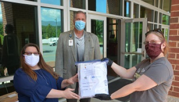 Two women hold up a package of masks while a man stands between them